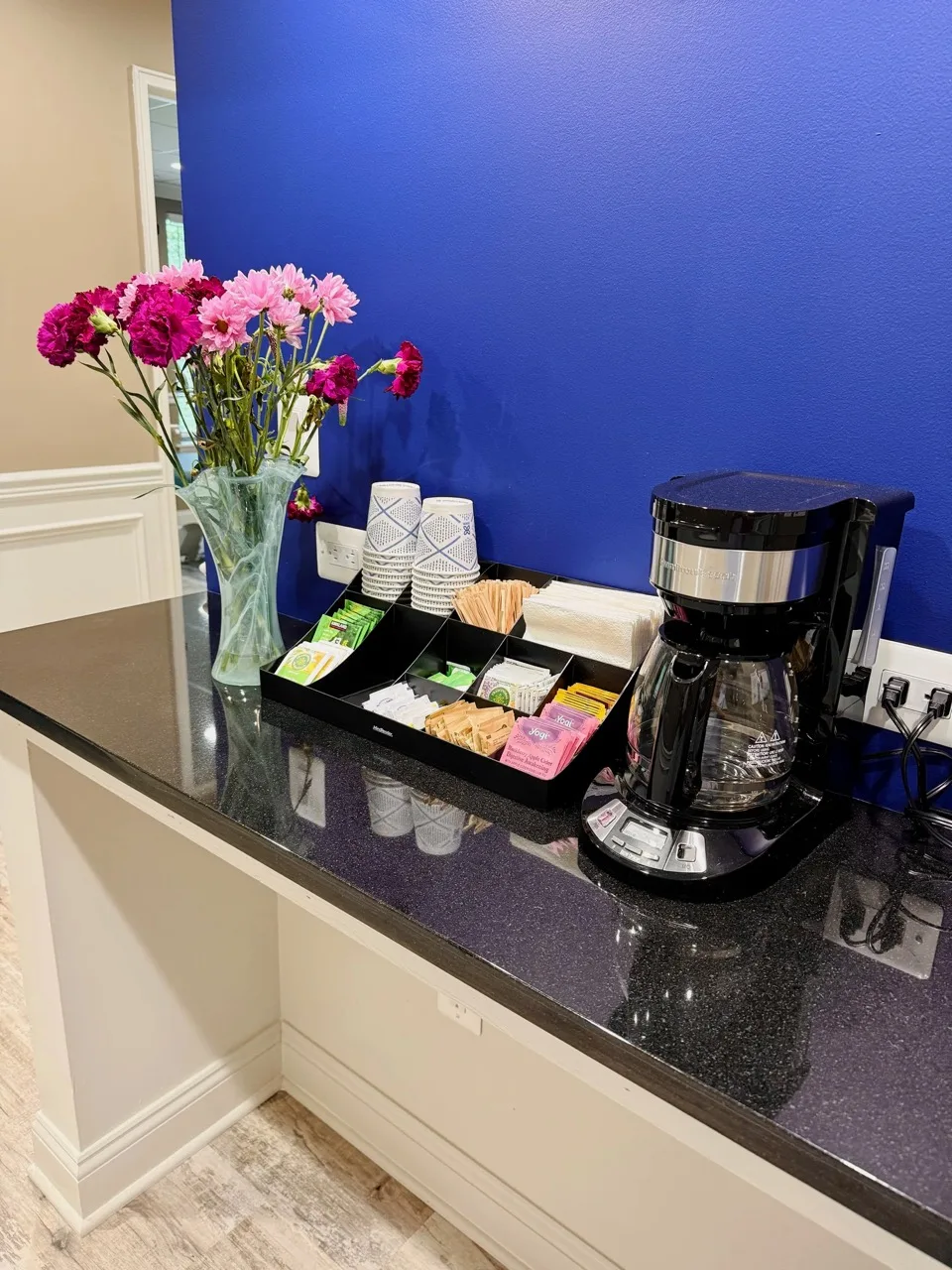 A small refreshment station with tea, coffee, and fresh flowers in the waiting area